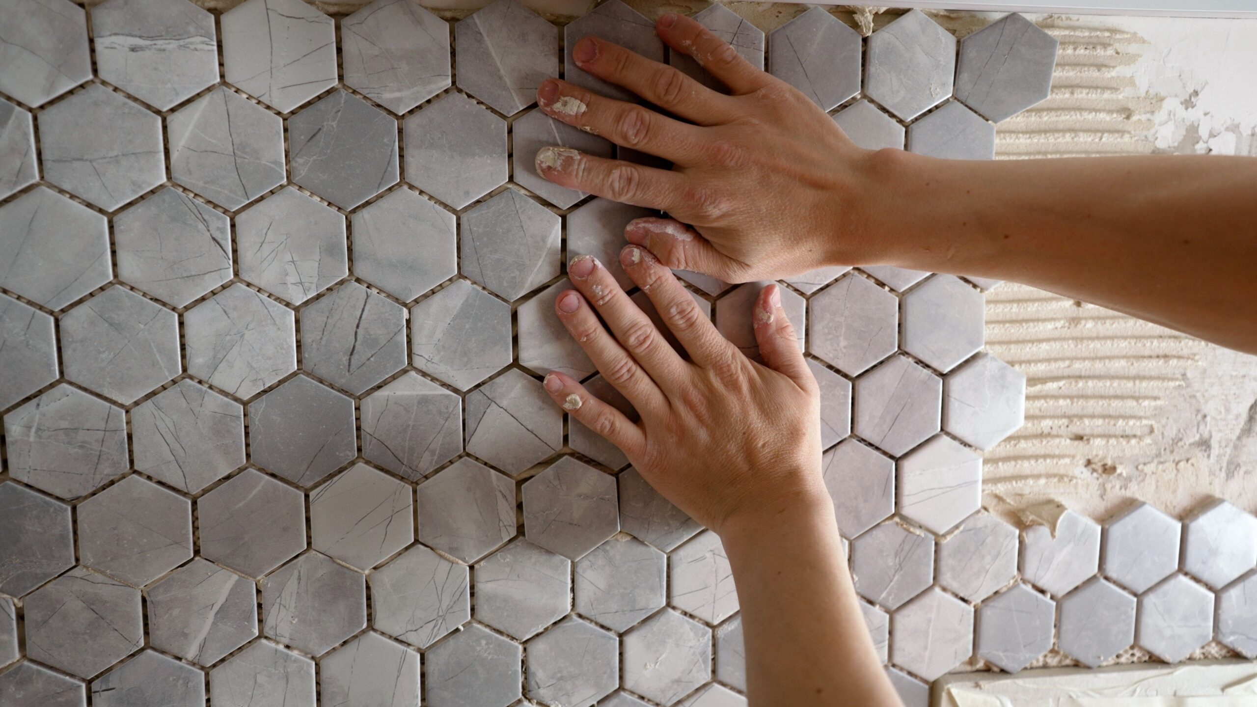 hands laying down honeycomb tile on bathroom wall